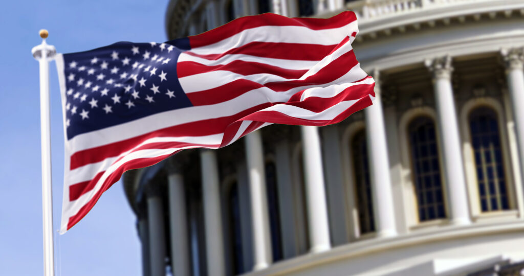 The flag of the united states of america flying in front of the capitol building blurred in the background. United states federal congress on Capitol hill in Washington D.C. Democracy and freedom.