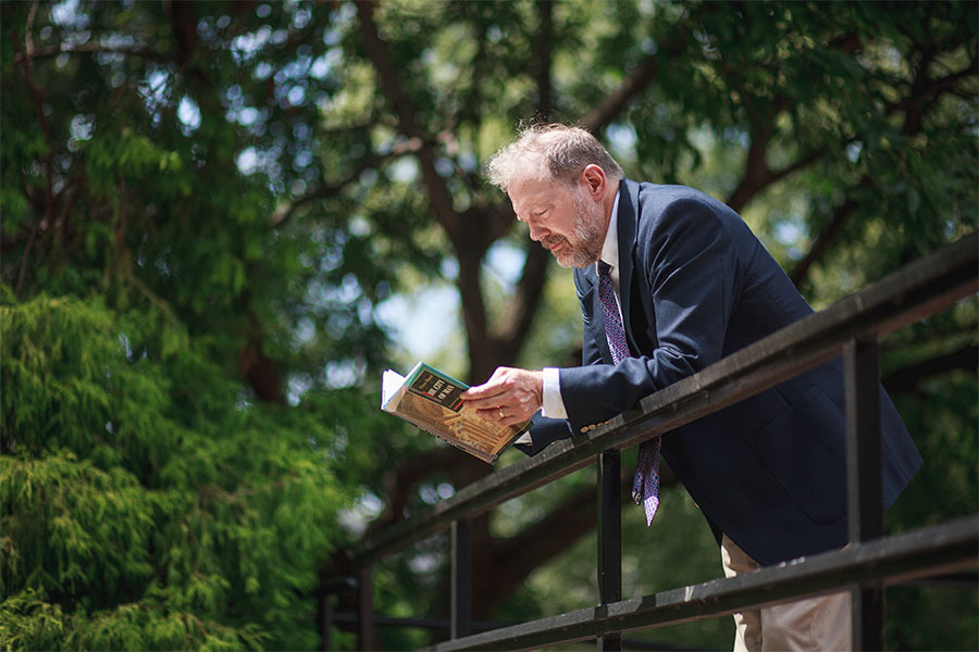 Dr. Nicholas Meriwether stands on a bridge reading a book on a sunny day