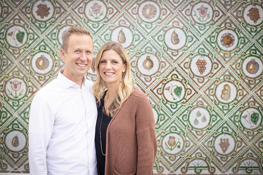 Jay and Sandy Smith are seen standing next to each other smiling in front of a wall