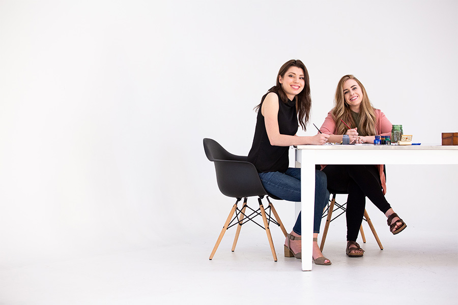 Artists Joanna Duka and Breanna Koski sit at a table working on a project