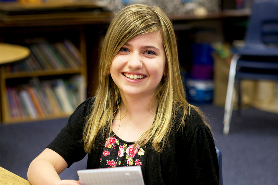 Katie Ayers sits at a desk in a school classroom smiling