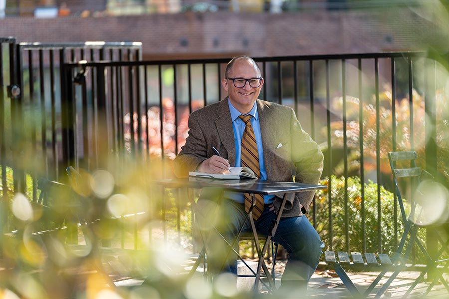 Peter Vlaming sits outside at a table writing in a notebook