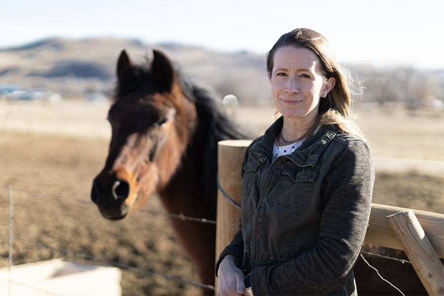 Jessica Bates stands against a fence with a horse in the background