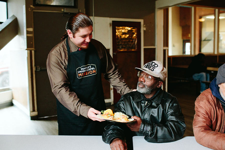 A worker with Seattle's Union Gospel Mission serves a meal to a homeless man