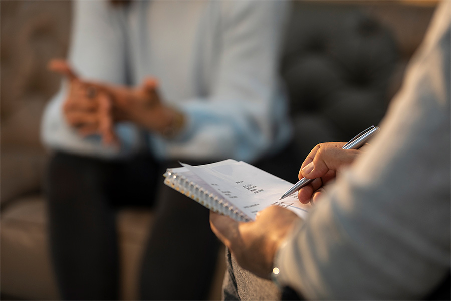 A counselor holds a clipboard of notes as he speaks with a client