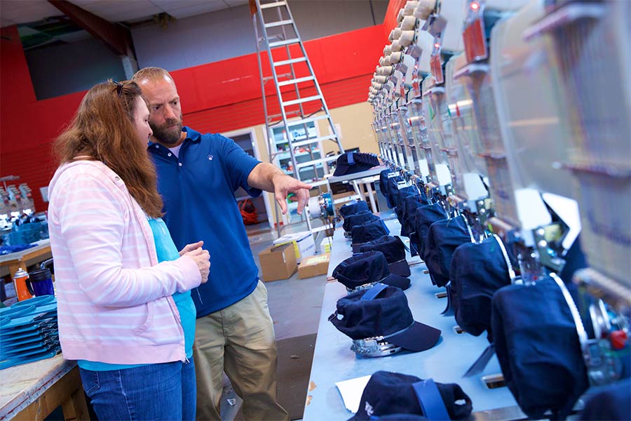 Blaine Adamson gestures toward a row of hats on a bench.